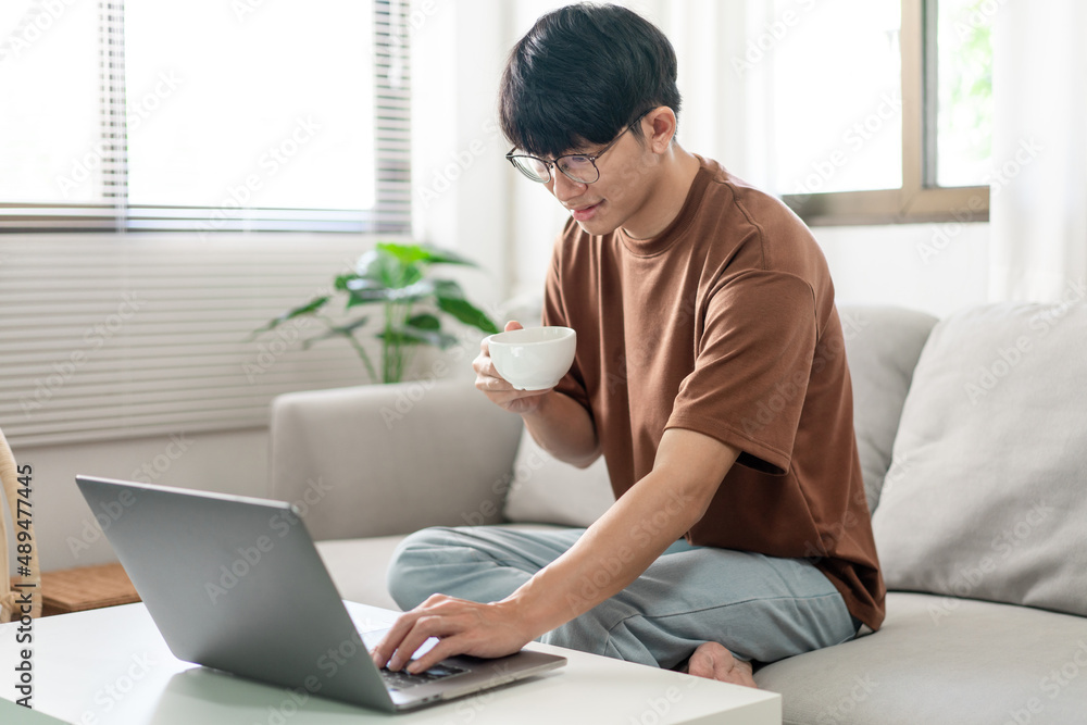 Technology Concept The man in brown T-shirt using one hand typing on his laptop while another hand holding a cup of coffee
