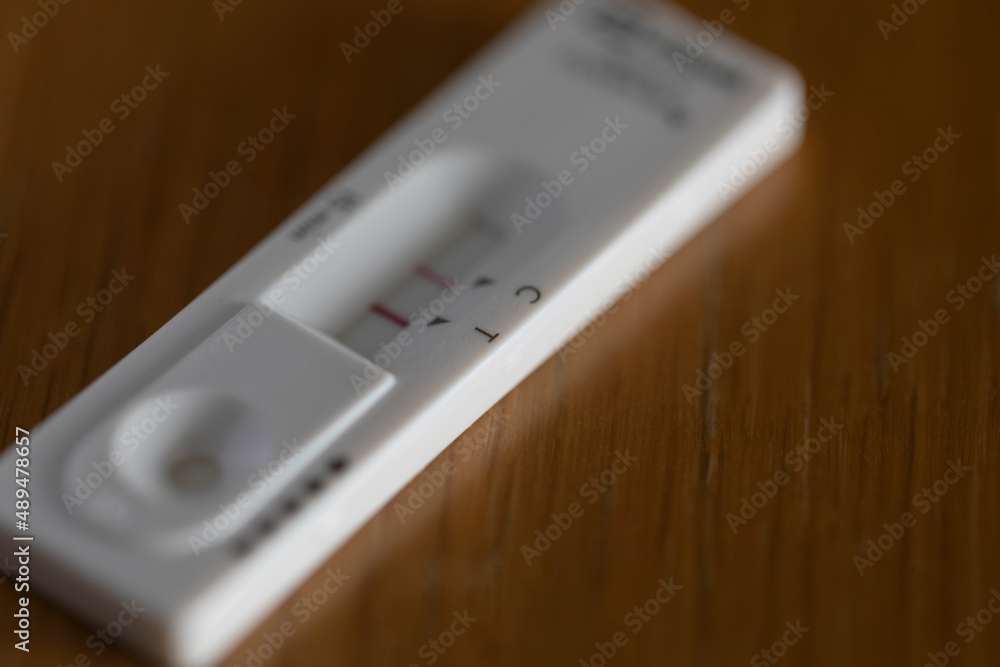 Covid rapid antigen test showing positive result on wooden table. Horizontal format with selective focus. Covid rapid antigen test showing positive result on wooden table. Horizontal format with selective focus.