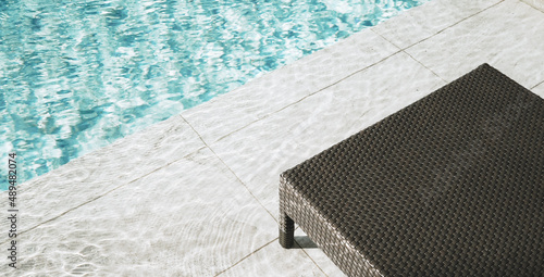 Fotografie Photo of Minimalist poolside scene featuring clear blue water next to a modern wicker lounge sunbed chair on a tiled deck, evoking relaxation and summer vibes