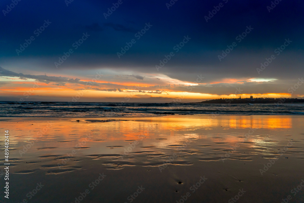 Scenic sunset on the ocean sandy beach with town silhouette on the horizon. Beautiful view landscape travel background. foorptints on sand.