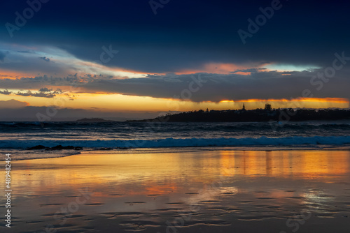 Scenic sunset on the ocean sandy beach with town silhouette on the horizon. Beautiful view landscape travel background. foorptints on sand. © Daria Nipot
