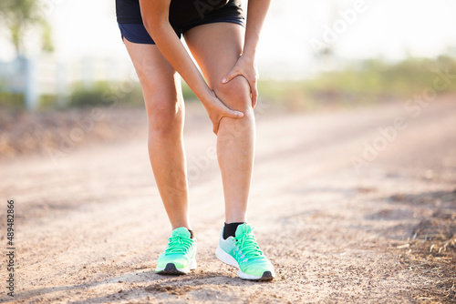 knee injury concept from exercise : Asian woman hands on knee while running on park road. Shot in the morning, sunlight and warm effects.