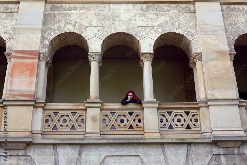 Full length portrait of red-haired woman wearing a  beautiful gothic gown costume, walking around  location with  romantic castle stone architecture background.