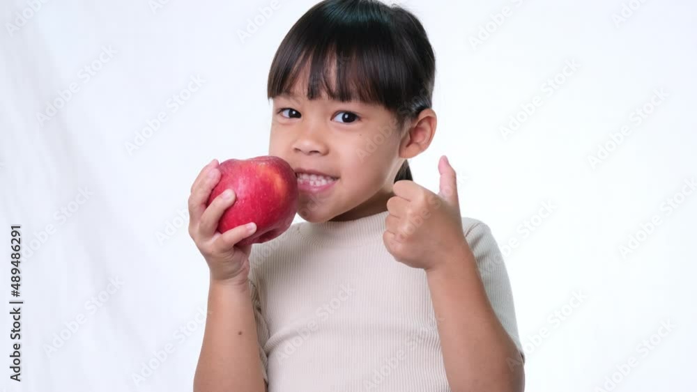 Happy little girl with apple. Cute Asian little girl eating organic apple on white background in studio. Healthy nutrition for small children. Happy little girl with apple. Cute Asian little girl eating organic apple on white background in studio. Healthy nutrition for small children.