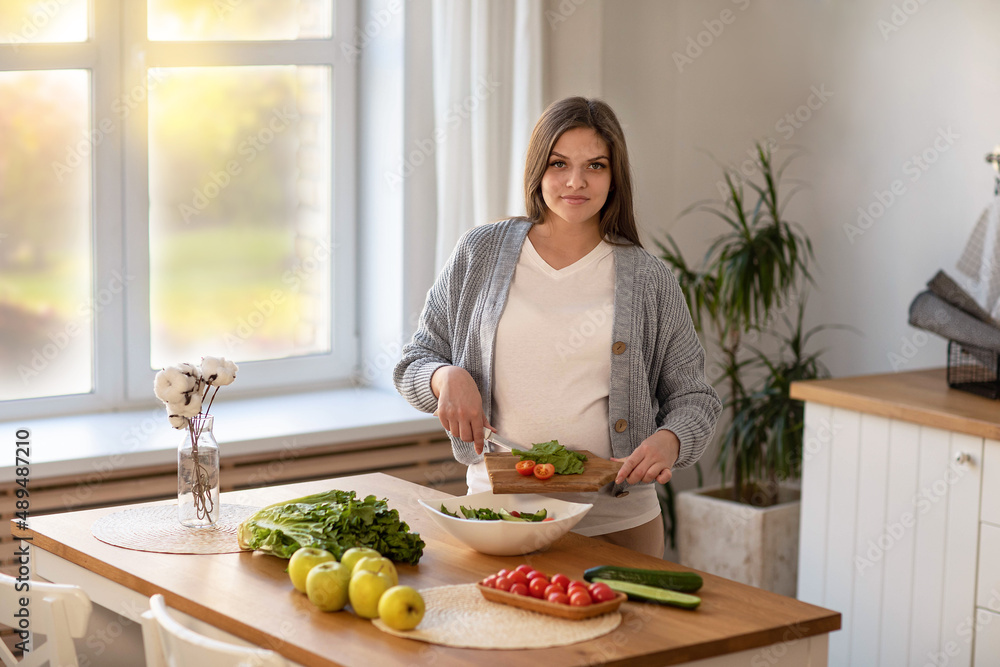 a young pregnant woman makes herself a salad of fresh vegetables, the concept of proper nutrition
