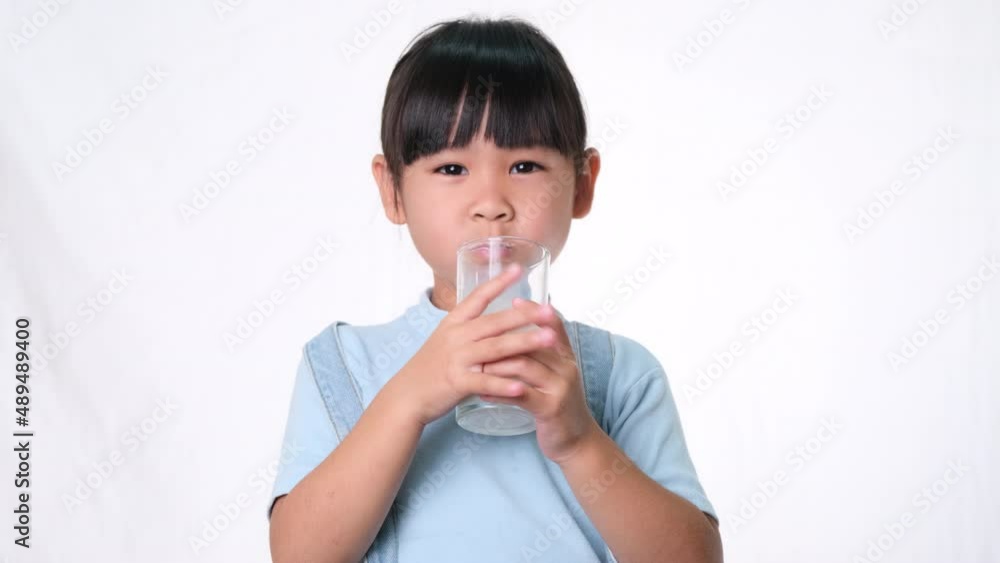 Asian little cute girl drinking milk from a glass and smile on white background in studio. Healthy nutrition for small children. Asian little cute girl drinking milk from a glass and smile on white background in studio. Healthy nutrition for small children.