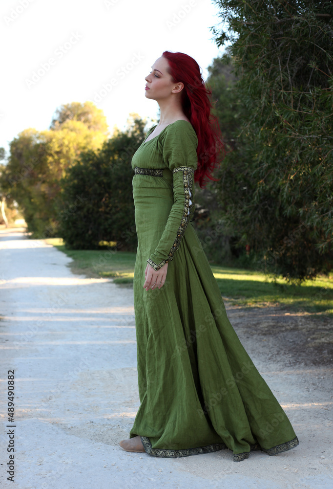 Full length portrait of red haired woman wearing a beautiful green medieval fantasy gown. Posing with gestural hands on a enchanted forest background. Full length portrait of red haired woman wearing a beautiful green medieval fantasy gown. Posing with gestural hands on a enchanted forest background.