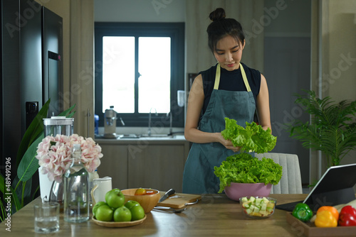 Young woman preparing ingredients for making healthy organic salad in kitchen. © Prathankarnpap