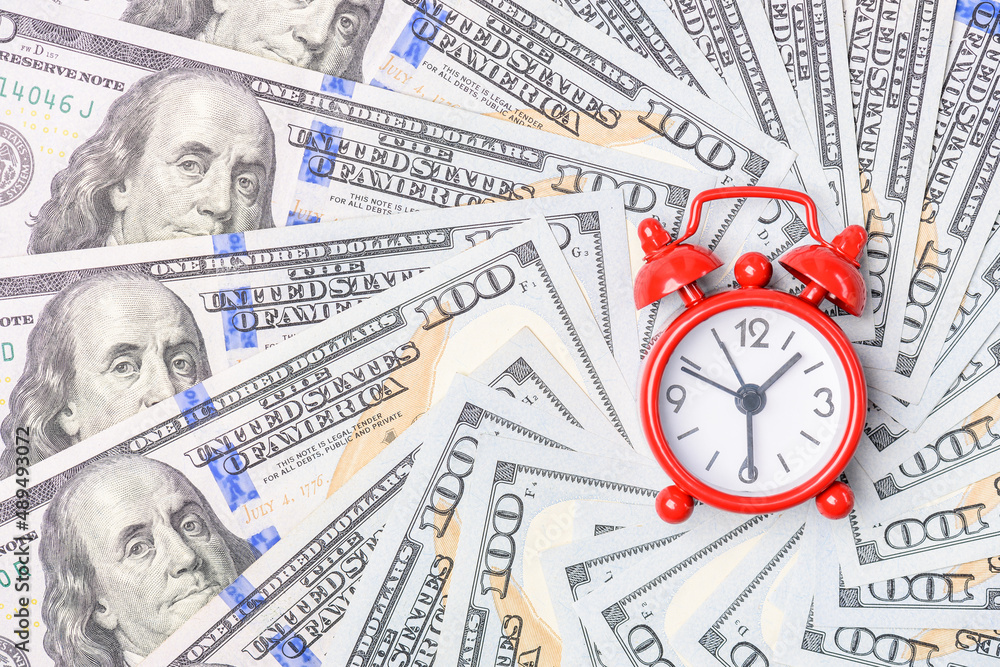 Time value of money concept : Red analog clock on US dollar banknote, depicting receiving money today can be poised to increase the future value by investing and gaining interest over a period of time Time value of money concept : Red analog clock on US dollar banknote, depicting receiving money today can be poised to increase the future value by investing and gaining interest over a period of time