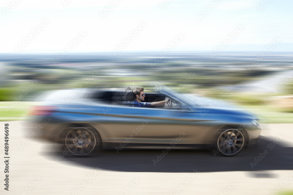 Hes a speed freak. A young man speeding on the open road in his silver convertable.