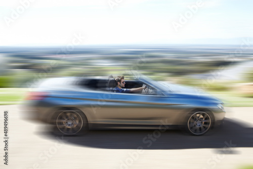 Hes a speed freak. A young man speeding on the open road in his silver convertable.