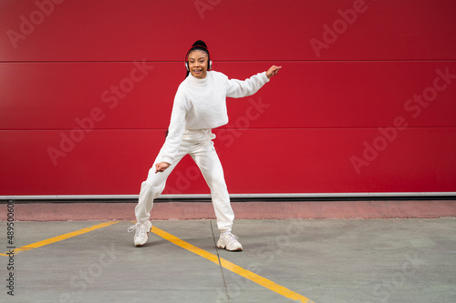 Cheerful African American woman with headphones dancing urban dance on a red background