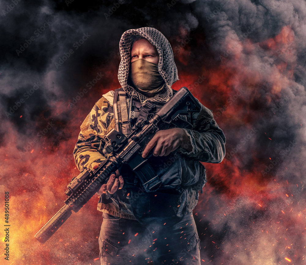 Modern army soldier with hood holding rifle against fire