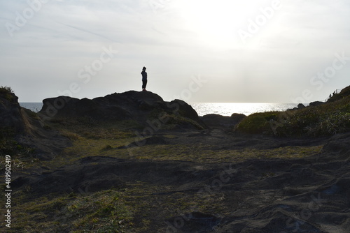 銀色の海と空黒い岩に立つビデオカメラを持った男性