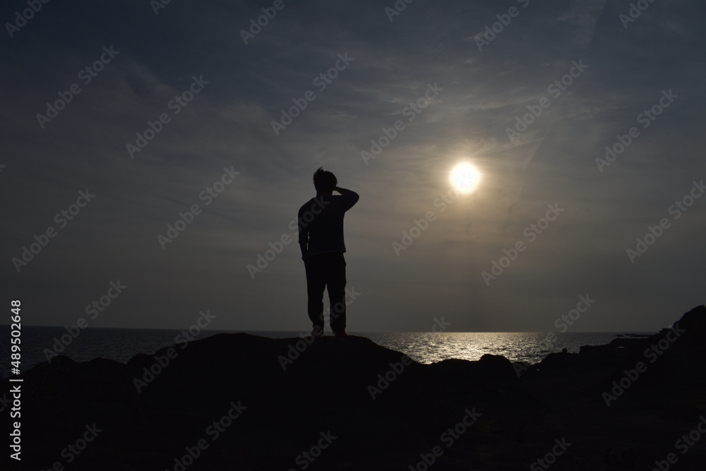 銀色の海と空黒い岩に立つビデオカメラを持った男性
