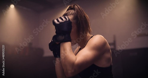 A Strong Kickboxing Woman Training On A Punching Bag In An MMA Gym. Shot In A Crossfit Boxing Gym With Low Key Lighting And A Scattering Of Haze. Captured On Red Digital Cinema Camera 