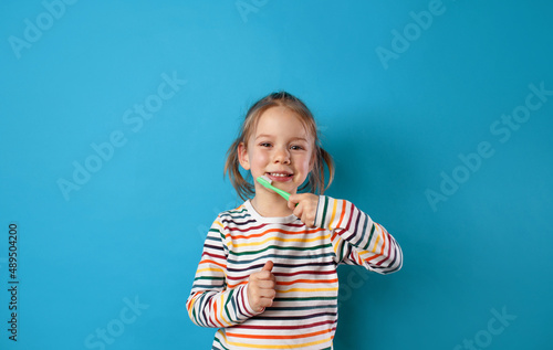 a little girl is brushing her teeth with a toothbrush on a blue isolated background.