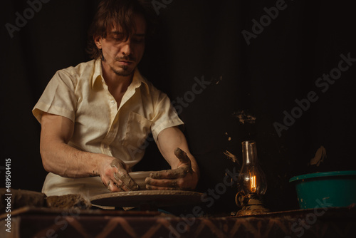 man in pottery workshop makes plate of clay, an authentic atmosphere, yellow lamp, lifestyle, magical atmosphere. Concept with your own hands, home entertainment. black background © Valeriia