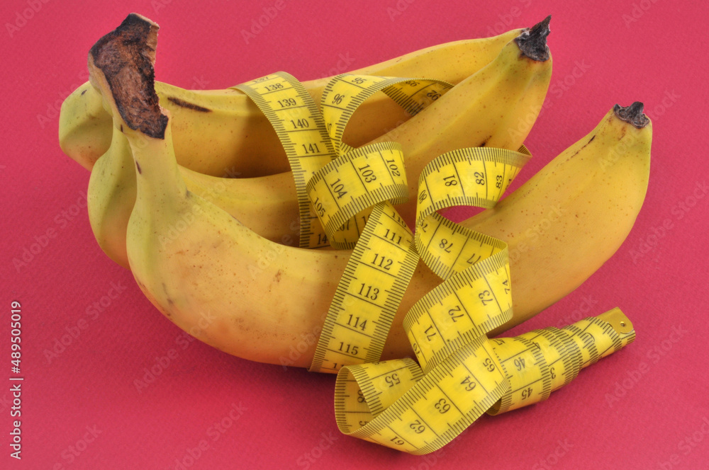 Concept de régime bananes avec un mètre souple sur un fond rouge Concept de régime bananes avec un mètre souple sur un fond rouge