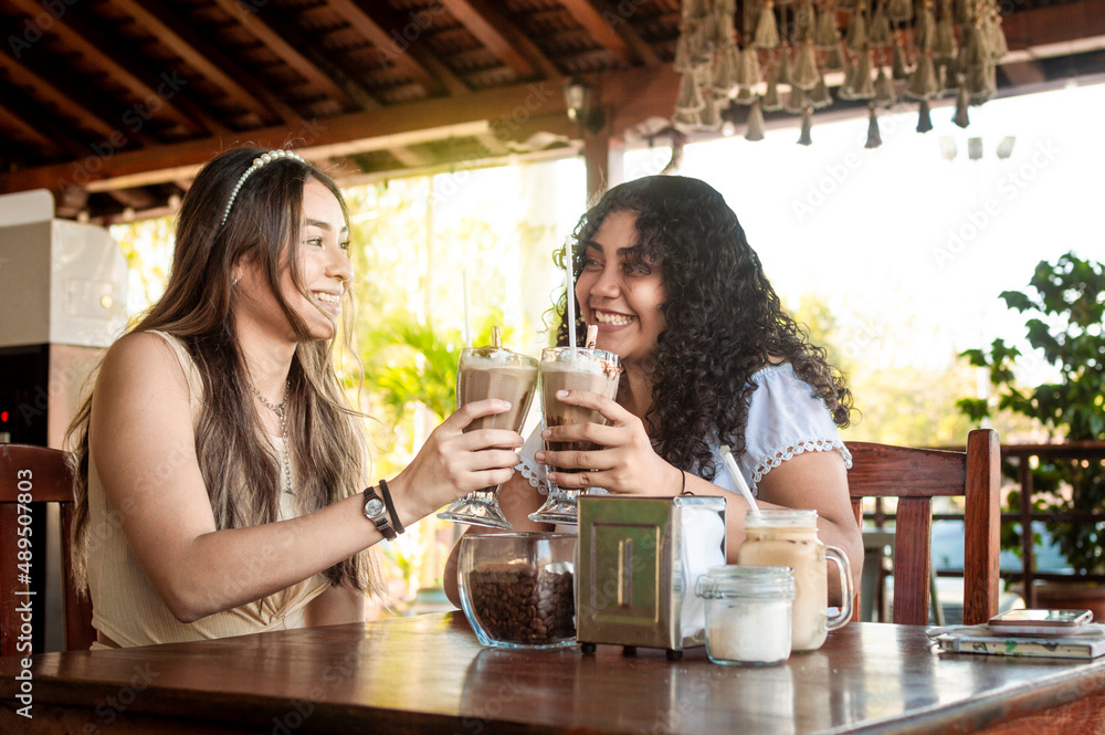 Two girls having a milkshake, two girl friends in a cafe, two girls toasting in a cafe Two girls having a milkshake, two girl friends in a cafe, two girls toasting in a cafe