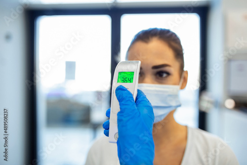 A pandemic workplace environment. Office workers wear face coverings to protect the spread of virus doing the Covid-19 / Coronavirus outbreak. Body temperature is checked with a infrared thermometer.