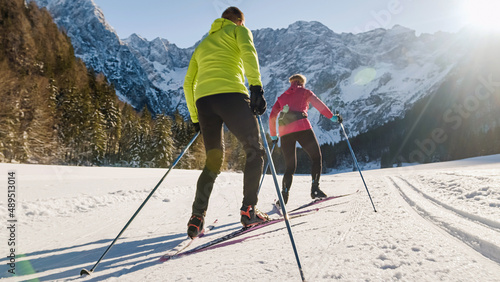 Bild auf Leinwand Caucasian couple recreational cross country skiing on snowy flat terrain, in the foothill of a beautiful stunning mountain, wide ground level shot