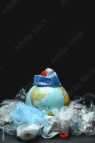 A globe of the world surrounded by plastic garbage on a black background. Concept of planet Earth pollution by plastic, polyethylene. Copy space