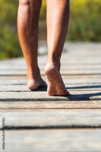 Barefoot woman walking on a wooden pier. Concept of nudism and naturism. Female people legs in clos eup. Summer holiday vacation and travel image. Defocused nature background © simona