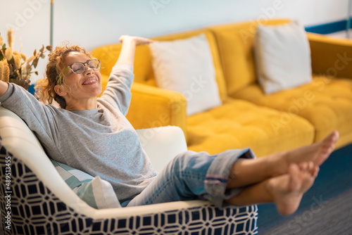 Happy young adult caucasian woman sitting on a chair at home in living room open her arms and smile a lot. Success and satisfaction lifestyle female people have relax leisure activity
