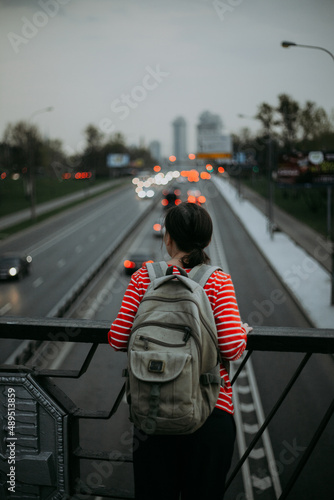 a girl in a red jacket looks at the highway with cars