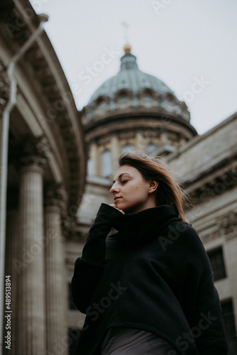 A young woman stands at a beautiful monumental building and looks away