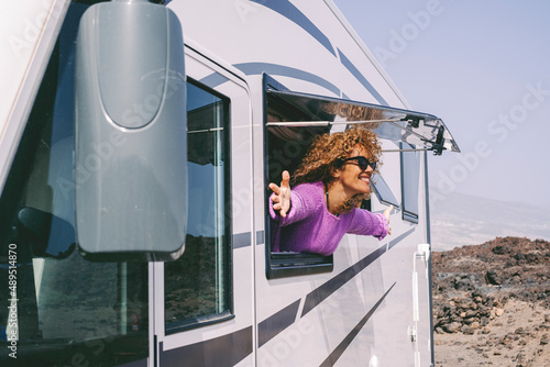 Overjoyed and excited adult pretty woman admire outside the camper van window and outstretching arms with big smile. Concept of tourist people and tourism with rented vehicle. Nature campsite