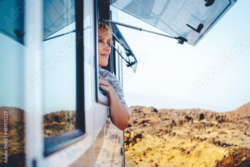 Nice adult woman smile and enjoy freedom at the natural campsite admiring outdoors outside the window of her camper car. Concept of summer tourist travel vacation and free female independence people