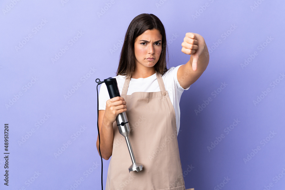 Brazilian woman using hand blender isolated on purple background showing thumb down with negative expression Brazilian woman using hand blender isolated on purple background showing thumb down with negative expression