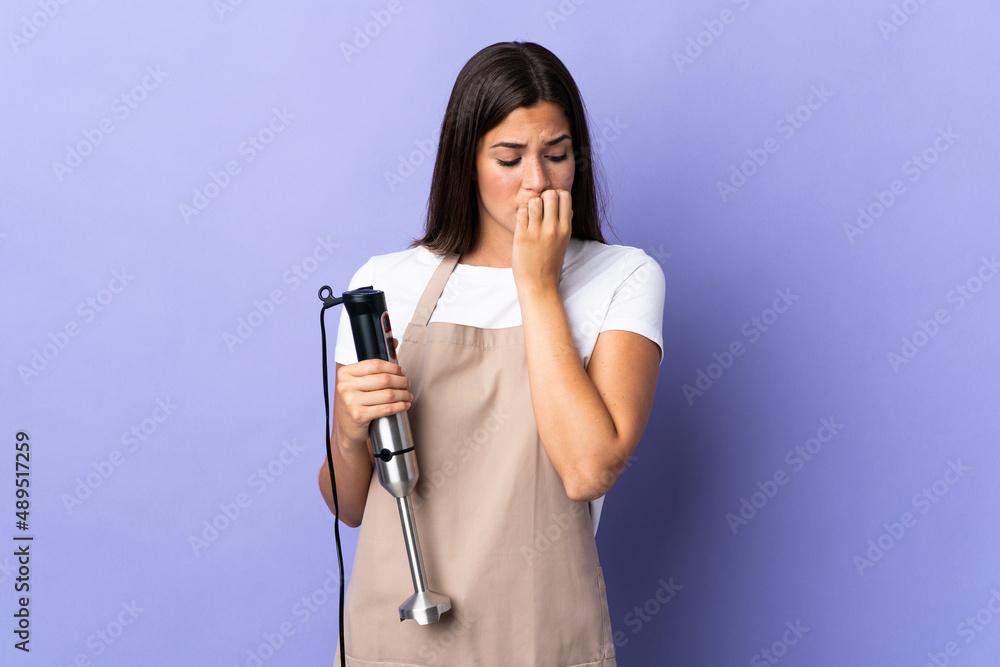 Brazilian woman using hand blender isolated on purple background having doubts Brazilian woman using hand blender isolated on purple background having doubts