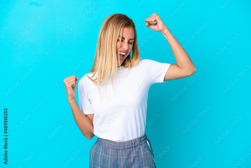 Blonde Uruguayan girl isolated on blue background celebrating a victory Blonde Uruguayan girl isolated on blue background celebrating a victory
