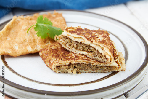 Crepes stuffed on plate, thin pancakes, blini, white wooden table