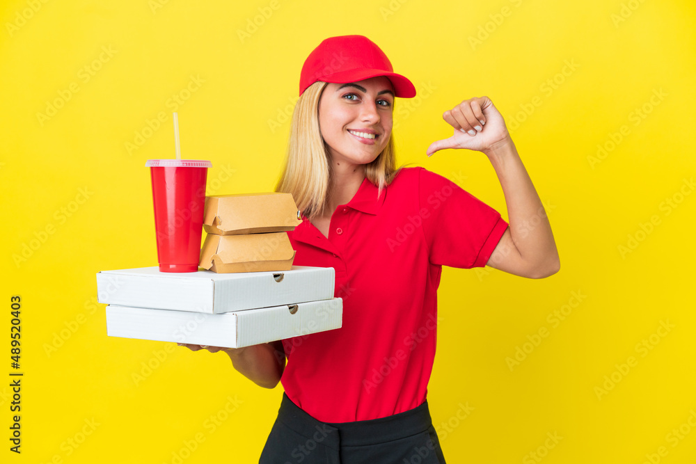 Delivery Uruguayan woman holding fast food isolated on yellow background proud and self-satisfied Delivery Uruguayan woman holding fast food isolated on yellow background proud and self-satisfied