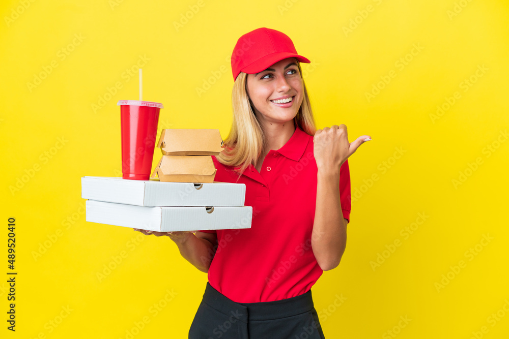 Delivery Uruguayan woman holding fast food isolated on yellow background pointing to the side to present a product Delivery Uruguayan woman holding fast food isolated on yellow background pointing to the side to present a product