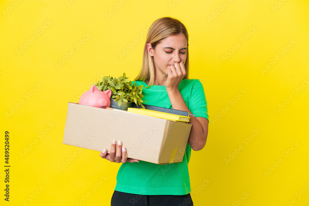 Young Uruguayan girl making a move while picking up a box full of things isolated on yellow background having doubts Young Uruguayan girl making a move while picking up a box full of things isolated on yellow background having doubts