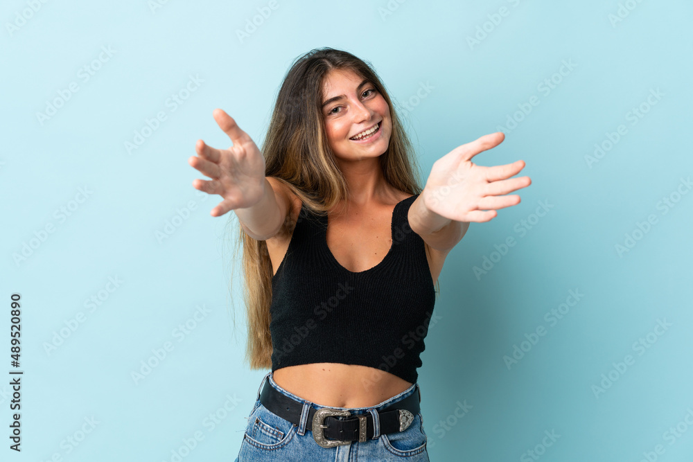 Young caucasian woman isolated on blue background presenting and inviting to come with hand Young caucasian woman isolated on blue background presenting and inviting to come with hand