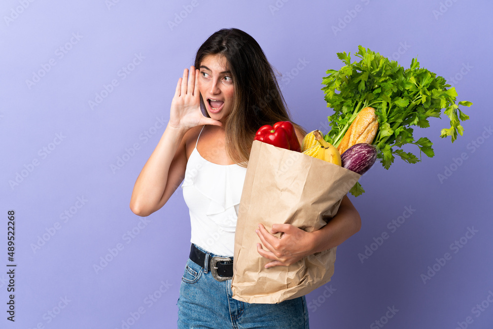 Young woman holding a grocery shopping bag shouting with mouth wide open to the side Young woman holding a grocery shopping bag shouting with mouth wide open to the side