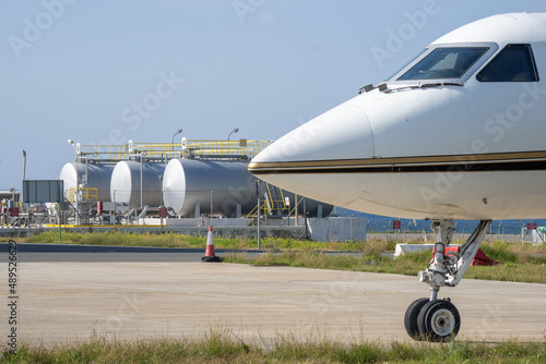 The nose of the aircraft against the background of fuel tanks at the airport.