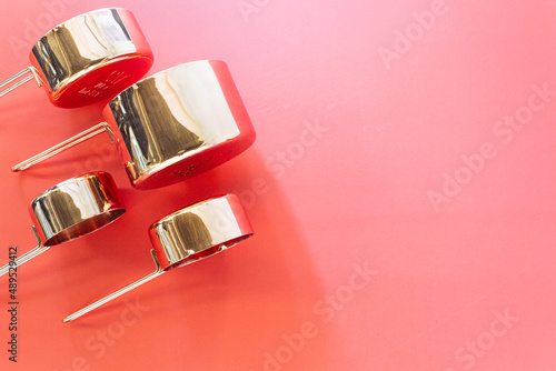 Collection of empty copper measuring cups on red background in top view