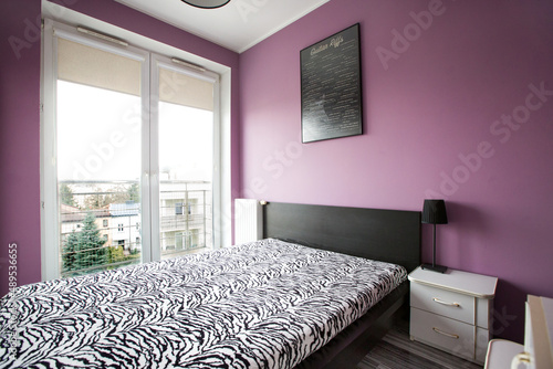Stylowa sypialnia z dużym łóżkiem i fioletowymi ścianami