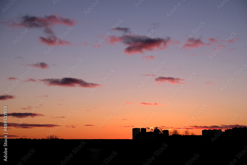 Landscape, with disturbing red sunset in the sky and few clouds above dark skyline and some buildings contours at far