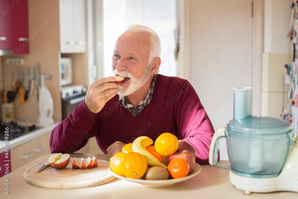 Senior man eating apple and other fruits in the kitchen on a sunny morning. Senior man eating apple and other fruits in the kitchen on a sunny morning.