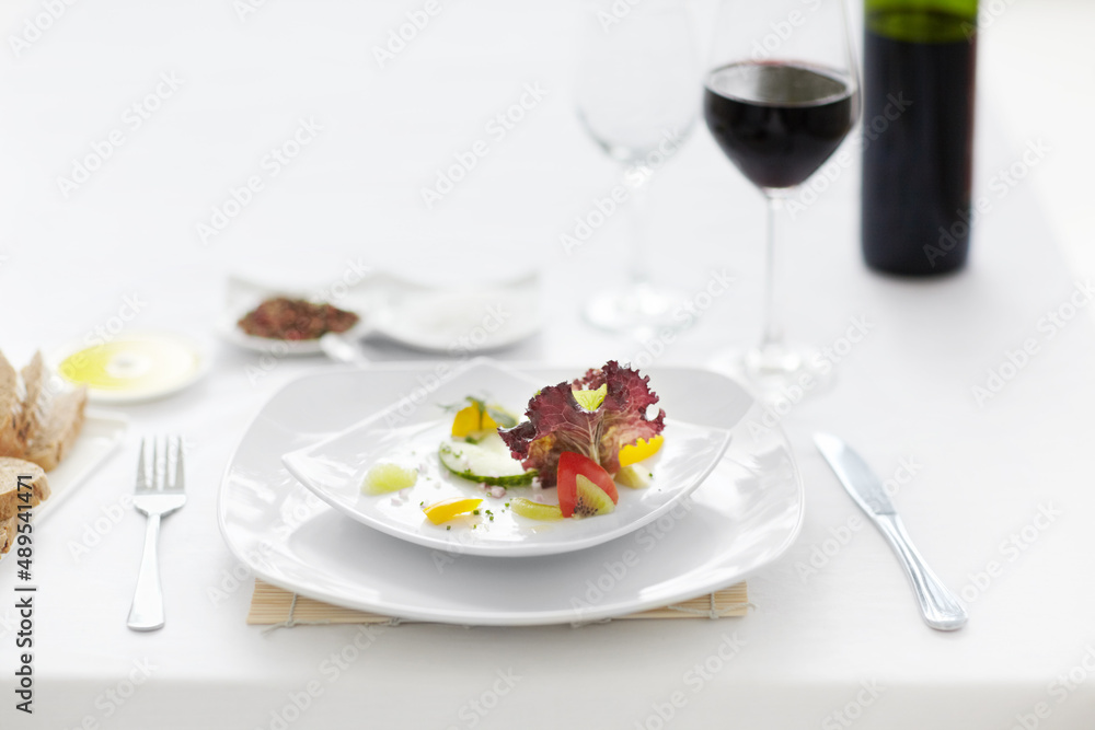 The picture of fine dining. A beautifully prepared salad accompanied by a glass of wine on a white table setting.