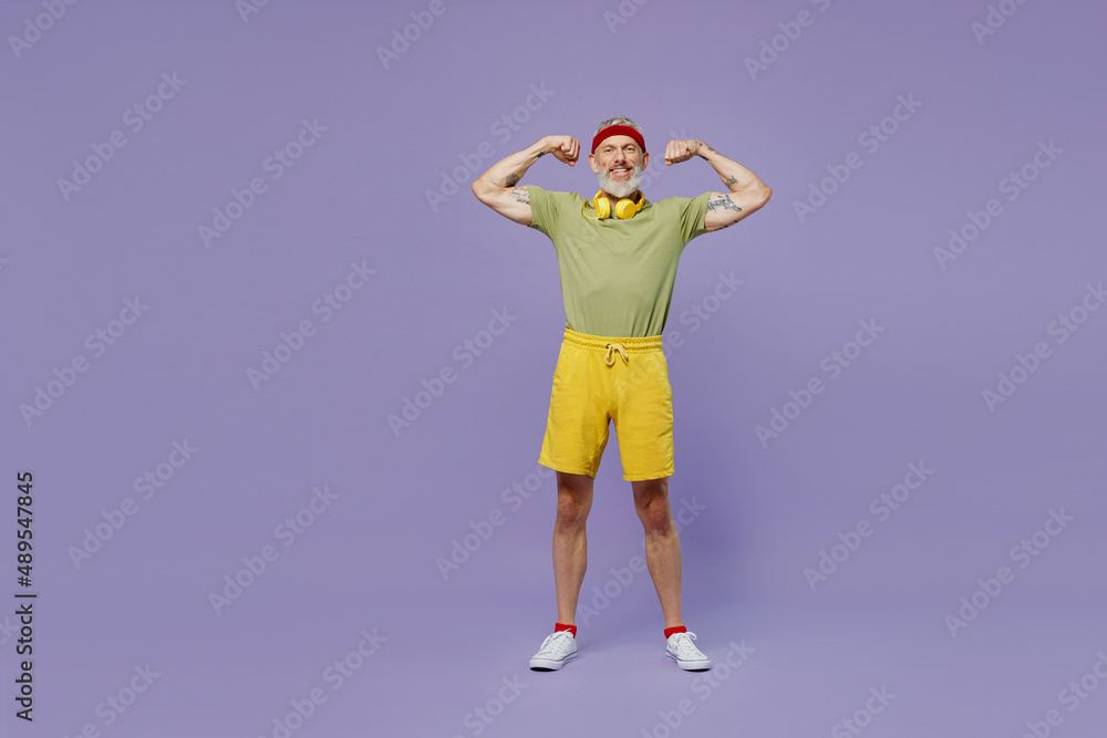 Full size body length elderly sporty gray-haired bearded man 40s years old in headband khaki t-shirt showing biceps muscles on hands isolated on plain pastel light purple background studio portrait.
