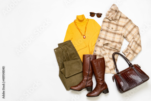 Female winter or autumn stylish clothing set. Plaid checkered shirt, yellow sweater and leather boots, green corduroy trousers, bag and sunglasses. Trendy fashionable casual clothes. Fashion concept